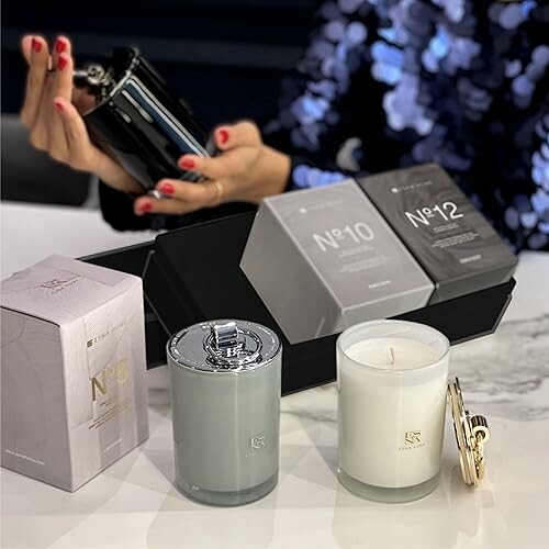 Person holding a perfume bottle with luxury candles and packaging on a table.
